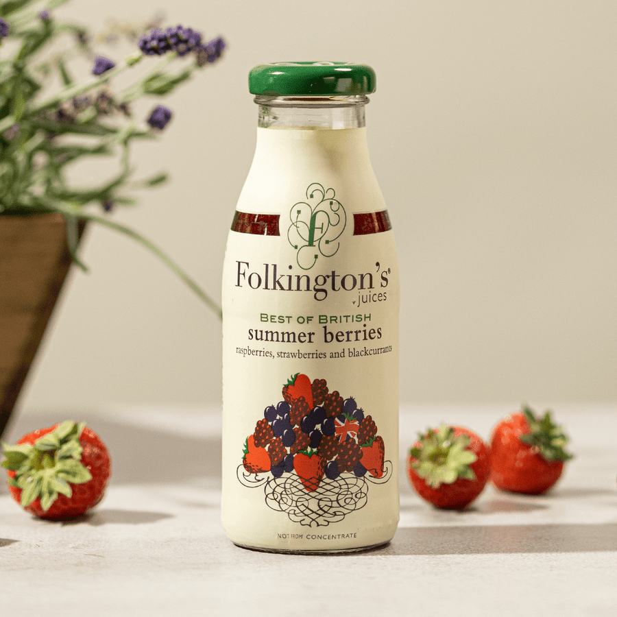 Image of 250ml Folkington's Summer Berries fruit juice standing on a table amongst scattered strawberries and a trug of lavender behind