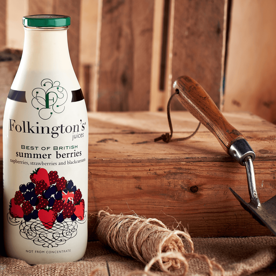 Lifestyle shot of a 1 litre bottle of Folkington's Summer Berries in a shed next to some garden twine and a fork.