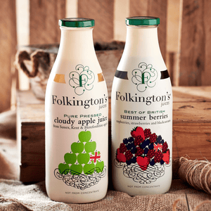 Lifestyle shot of a 1 litre bottle of Folkington's Summer Berries alongside a bottle of Apple Juice in a shed next to some garden twine and a trug