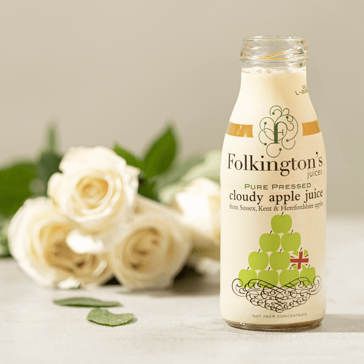 Open bottle of 250ml Apple Juice on a counter with a bunch of white roses and green leaves laying in the background.